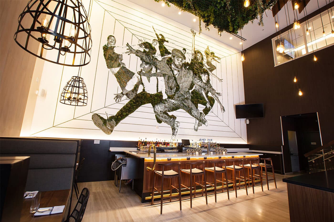 A hotel bar and dining room beneath a double-height wall mural made of preserved moss.