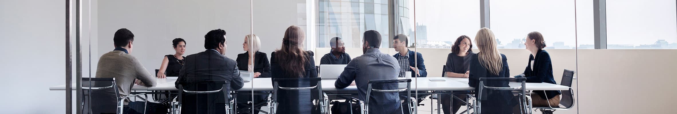 A team meeting around a long table in a glass-walled boardroom overlooking the city.