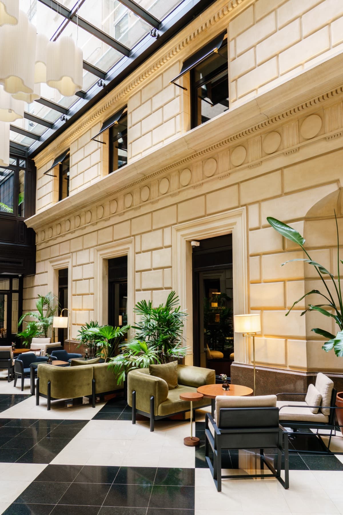 The glass-roofed atrium lobby at Casa Lucía in Buenos Aires, with green velvet seating on a chequered marble floor.
