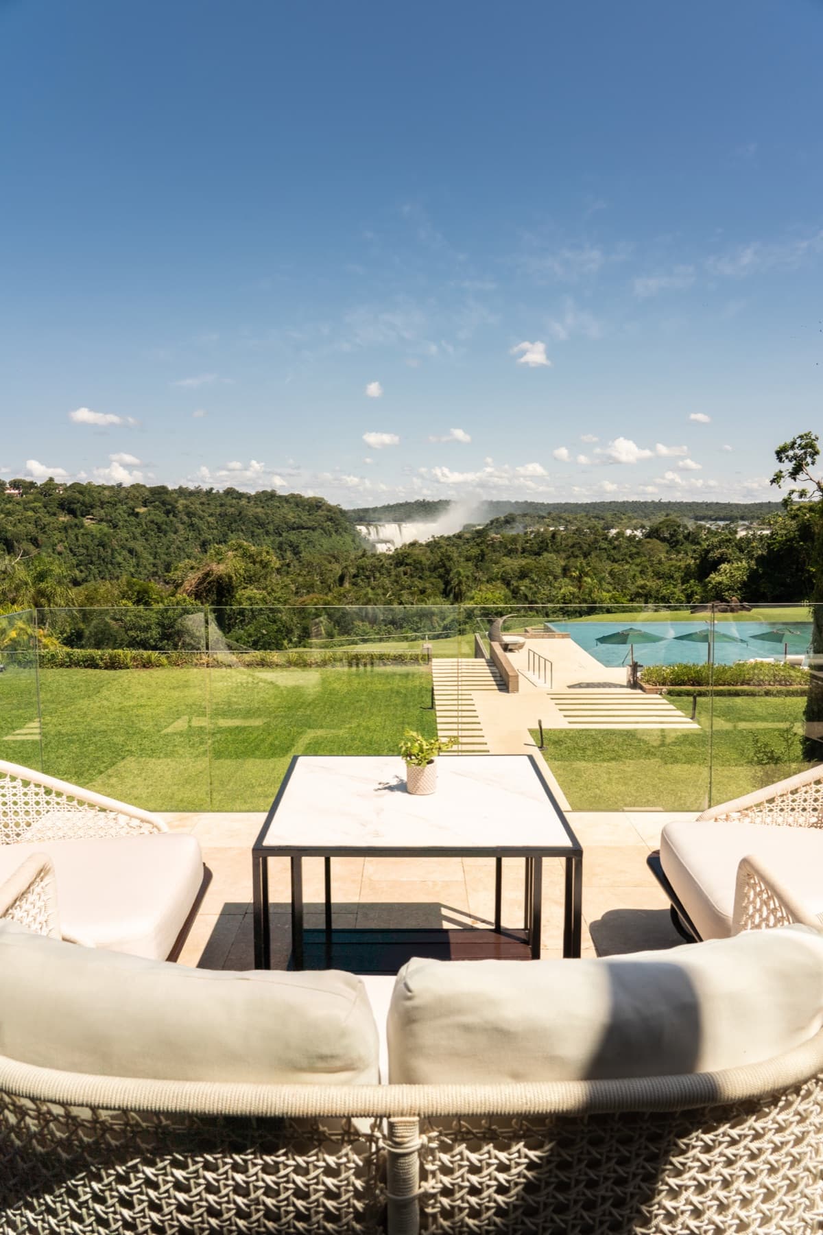 Terrace seating at the Amaro Bar, Gran Meliá Iguazú, looking across lawn and pool to the mist of the Iguazú Falls rising from the rainforest.