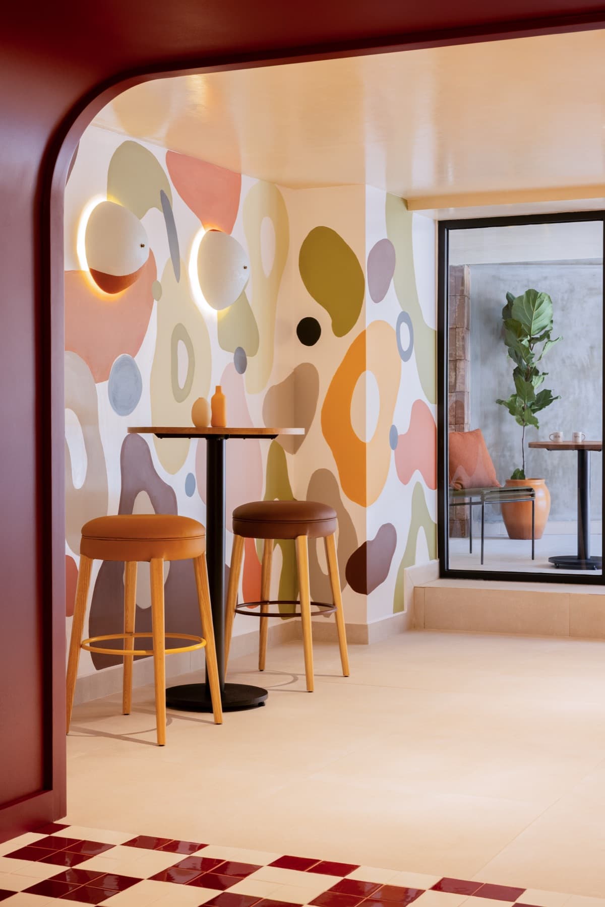 A bar nook at INNSIDE Mexico City Roma Norte, set against a pastel abstract mural beside a terracotta archway.
