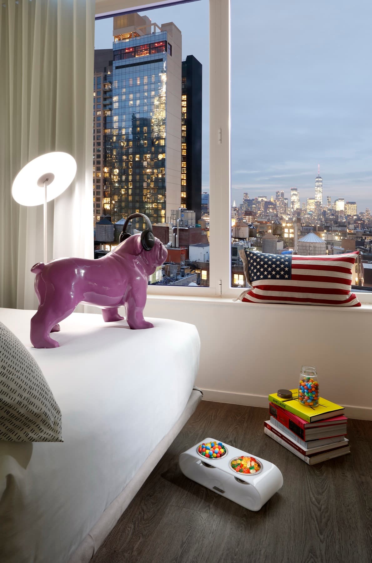 A king room at INNSIDE New York NoMad at dusk, its corner window framing the Manhattan skyline.