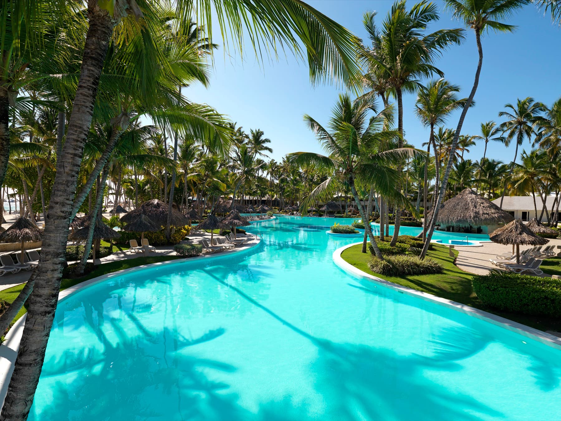 The winding main pool at Meliá Punta Cana Beach, edged with palms and thatched parasols.