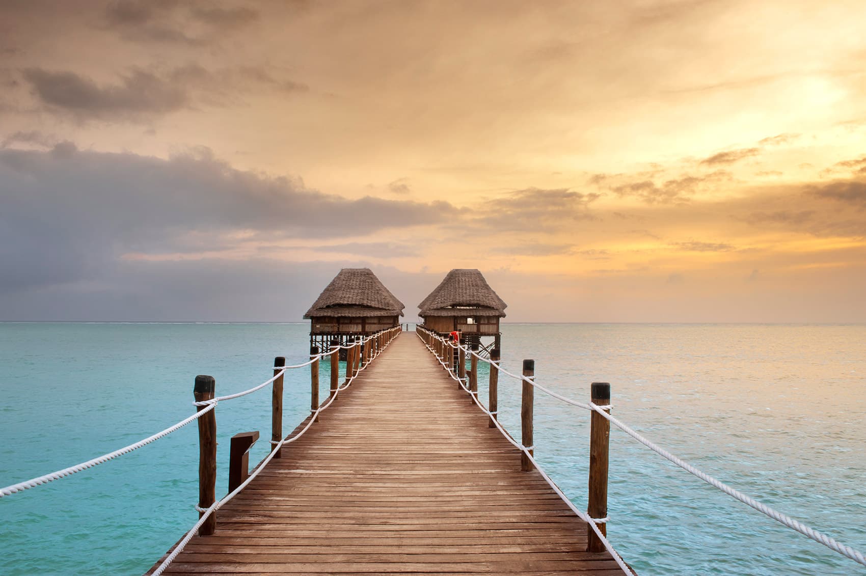 A wooden jetty leading to thatched overwater pavilions at sunset, Meliá Zanzibar.